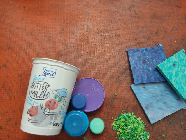Ein leerer Butter-Milch-Becher, bunte Deckel und Platten aus altem Plastik