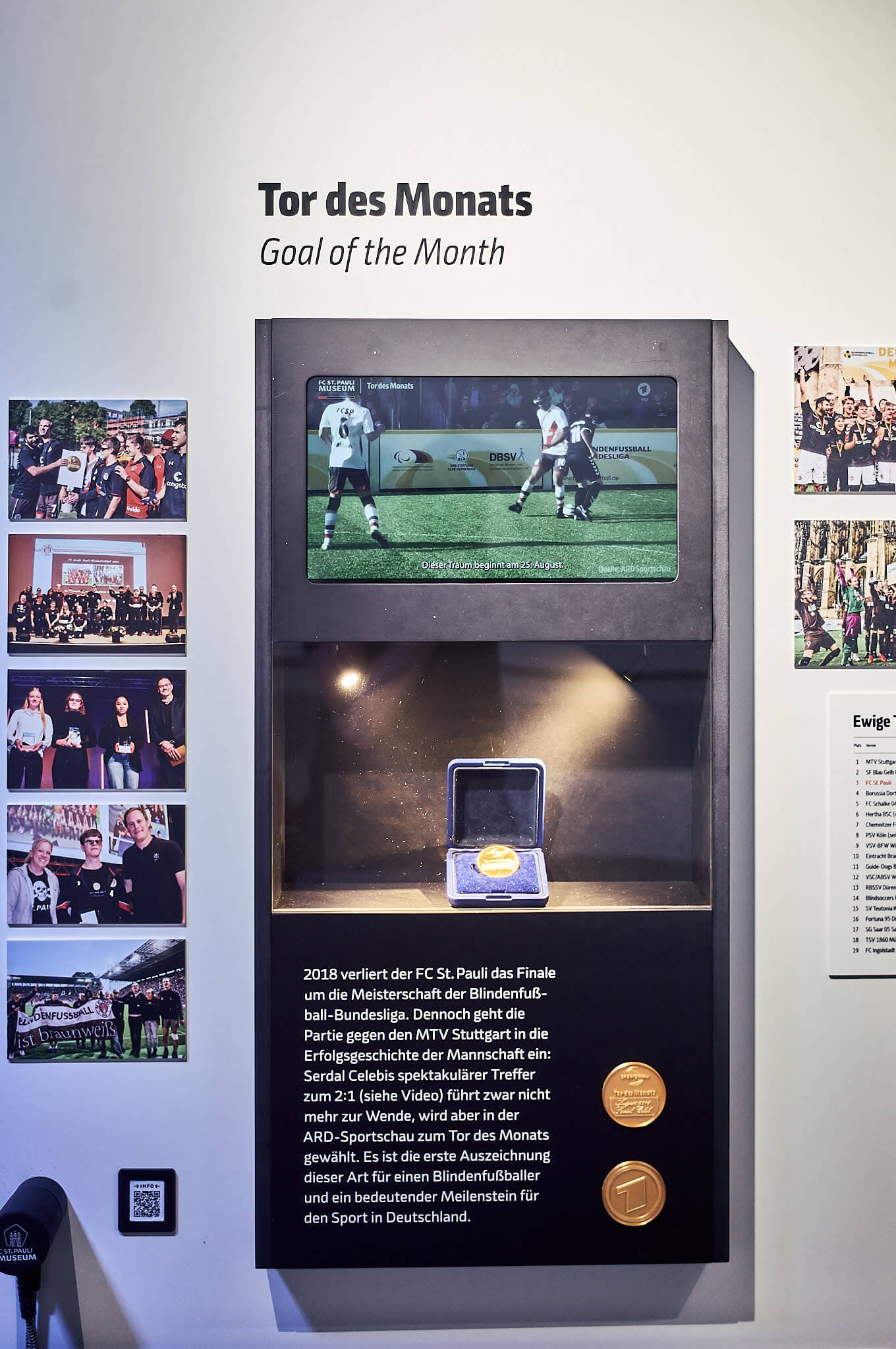 Ausstellungsvitrine „Tor des Monats“ im FC St. Pauli-Museum mit einer Medaille, einem Bildschirm und Informationen über das Tor von Serdal Celebi.